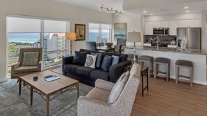 A modern living room with a dark-colored sofa, a wooden coffee table, and a patterned armchair. A ceiling fan and a view of the ocean are visible. - Inviting 2 Bedroom Condo – SanDestin Golf and Beach Resort (Miramar Beach)
