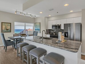 Una cocina moderna con una isla grande, electrodomésticos de acero inoxidable y vista al océano.