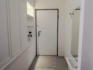 A narrow hallway with a white door, a white cabinet with a small shelf, and a white bathtub in the corner.