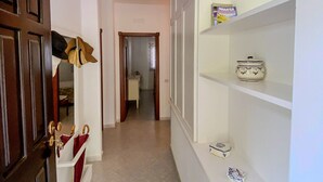Un pasillo con una puerta de madera, un perchero con sombreros y una estantería con utensilios de cocina.