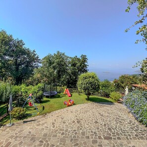 A garden with a stone pathway, a trampoline, and a slide.