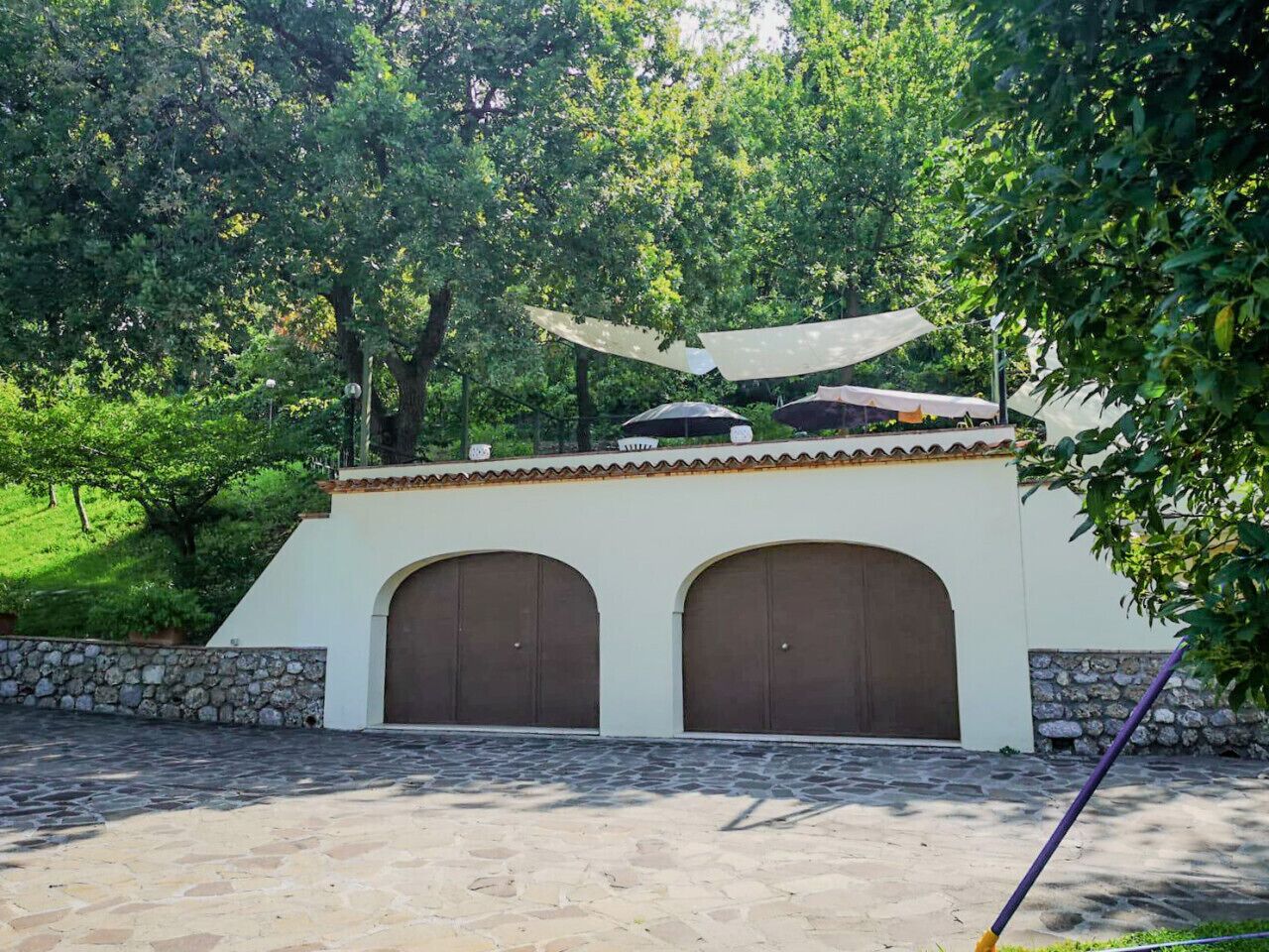 A building with two arched doors, a stone wall, and a paved area.
