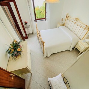 A bedroom with a bed, bedside tables, a dresser, a mirror, and a window with a view of greenery.