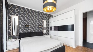 Ein modernes Schlafzimmer mit Wandgestaltung im geometrischen Muster, einem großen Bett, einem Kleiderschrank und einer Pendelleuchte.