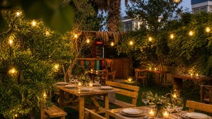 An outdoor dining area with wooden tables and benches, string lights, and candles. - Granma Butik Apart Otel (Bodrum)