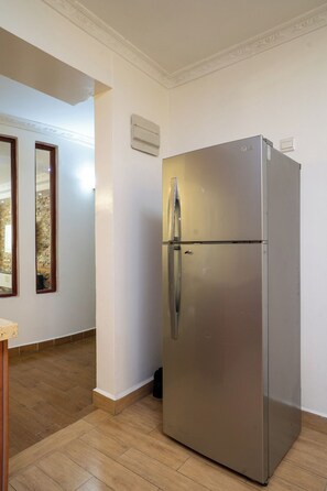 A stainless steel refrigerator in a hallway with a wooden floor and white walls. - Luxurious 4 Bedroom Apartment With a Rooftop Pool in Kilimani (Nairobi)