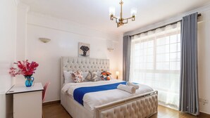 Hotellihuone, jossa on suuri sänky, työpöytä, maljakko täynnä kukkia ja ikkuna, jossa on verhot.