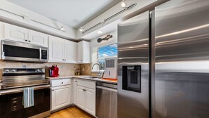 A modern kitchen with stainless steel appliances, white cabinetry, and a wooden floor. - Oceanfront 3BR Condo • Pool & Panoramic Views (New Smyrna Beach)