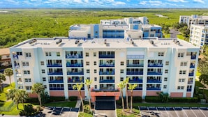 A multi-story hotel with balconies, a parking lot, and a view of a green landscape. - Oceanfront 3BR Condo • Pool & Panoramic Views (New Smyrna Beach)