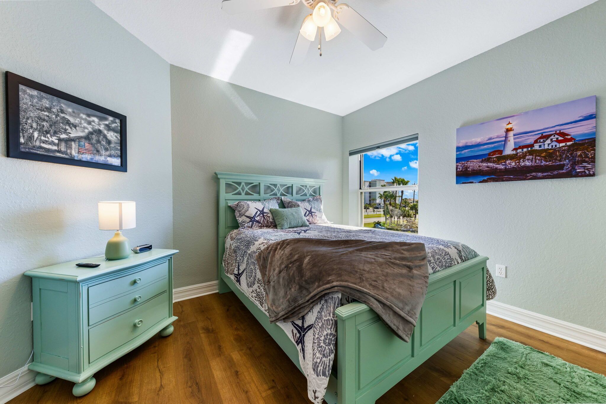 A bedroom with a bed, a nightstand, a lamp, and a window with a view.