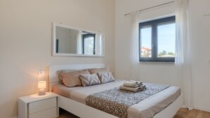 A bedroom with a bed, a bedside table with a lamp, a window with curtains, and a mirror on the wall. - Vila PrivePolai by Villas Guide (Pula)