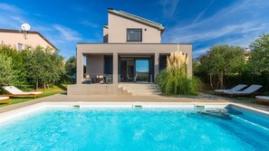 A modern house with a swimming pool, a patio with lounge chairs, and a view of the surrounding greenery. - Vila PrivePolai by Villas Guide (Pula)