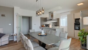 A modern kitchen with a central island, stainless steel appliances, and a dining area with a grey table and chairs. - Vila PrivePolai by Villas Guide (Pula)