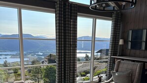 A cozy living room with a large window offering a scenic view of mountains and a lake. There is a sofa, a coffee table, and a lamp. - Chalet /Hytte with dream view, pure relaxation in the beautiful nature (Telemark)