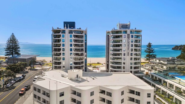 Ein modernes Hotel mit geschwungener Fassade, mehreren Balkonen und Blick auf Strand und Meer.