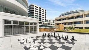Ein großes Schachbrett im Freien auf einem Innenhof, im Hintergrund moderne Gebäude.