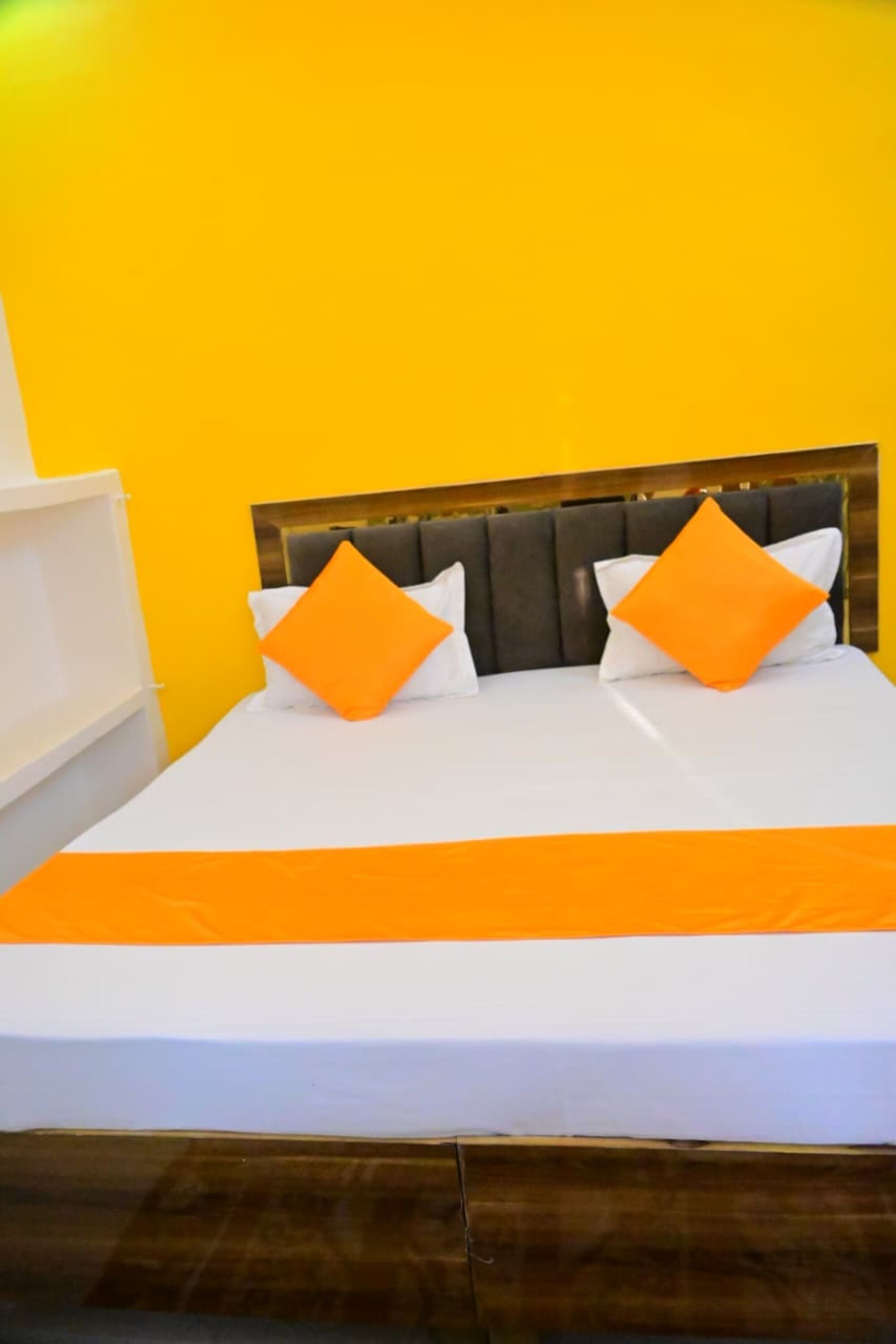A bed with a wooden headboard, two orange pillows, and a white bedspread.