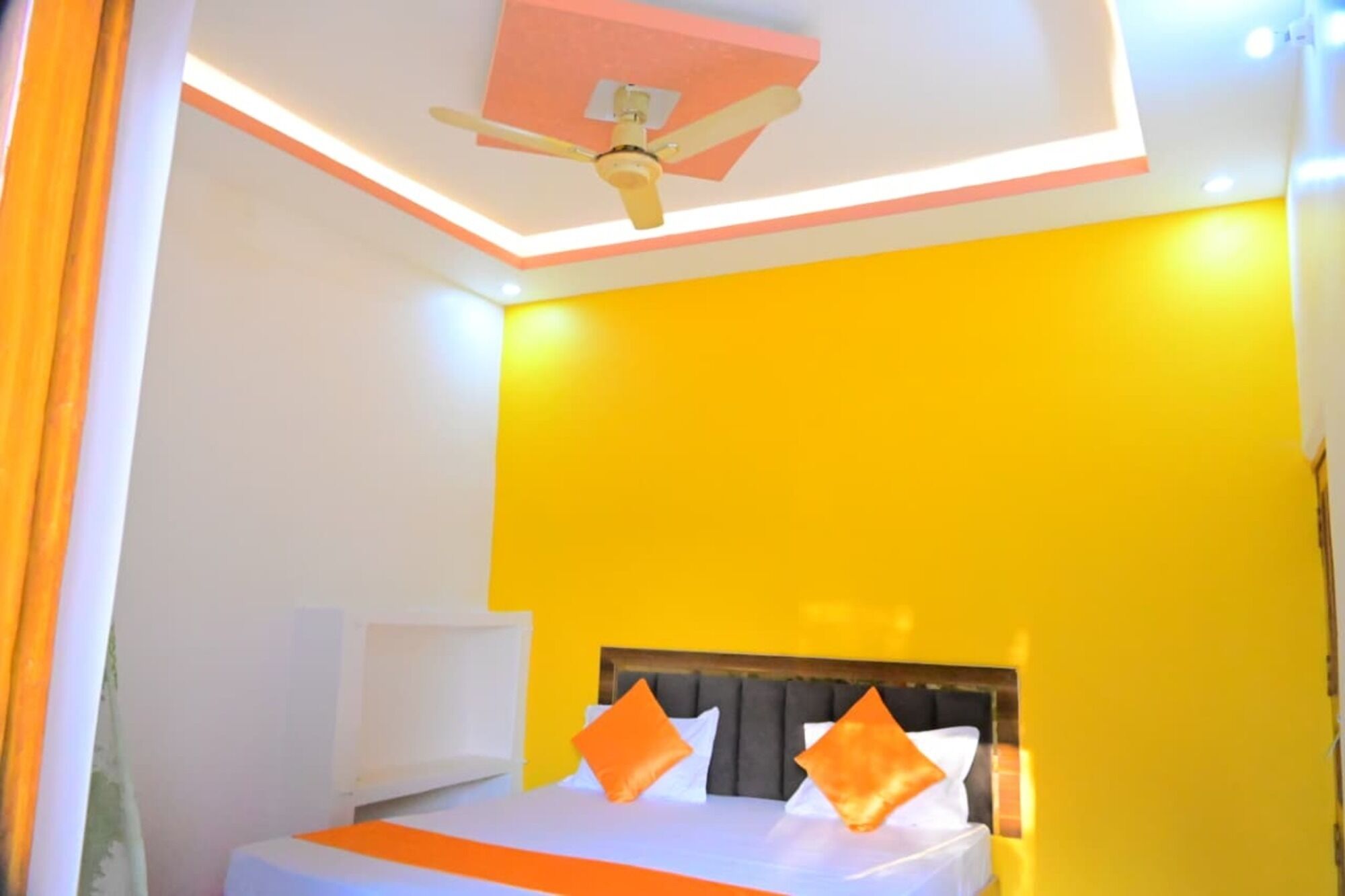 A hotel room with a bed, a ceiling fan, and a bright yellow wall.