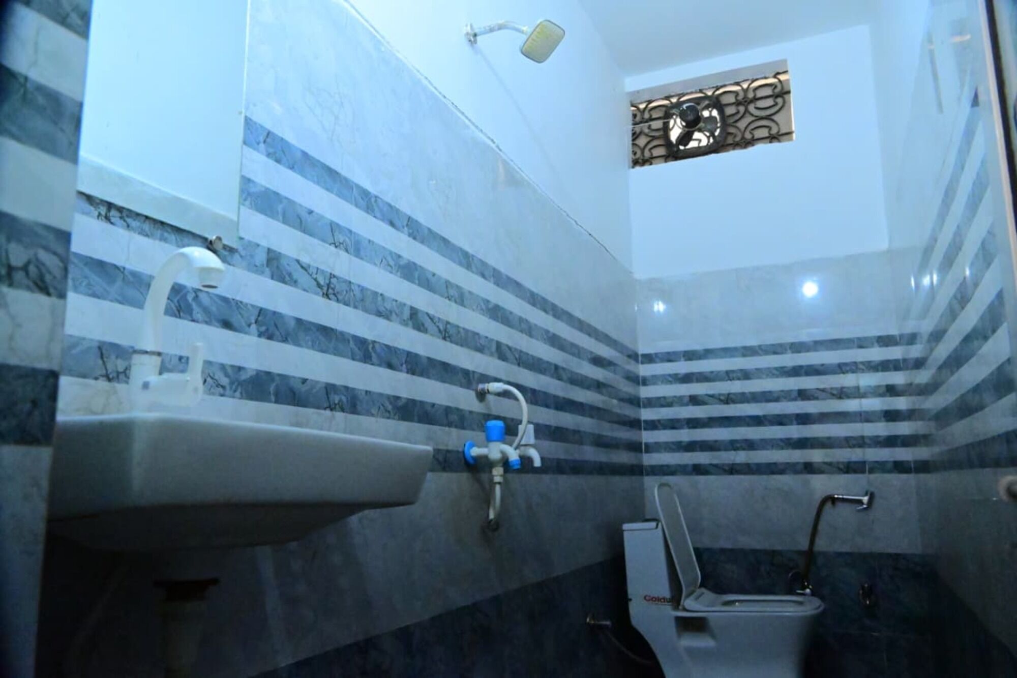 Une salle de bain avec un mur décoré d’un motif imitant le marbre, un lavabo, des toilettes et une douche.
