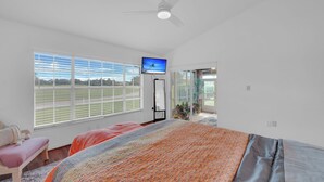 Ein Schlafzimmer mit einem großen Bett, einem Fernseher und Blick auf ein Sportfeld durch das Fenster.