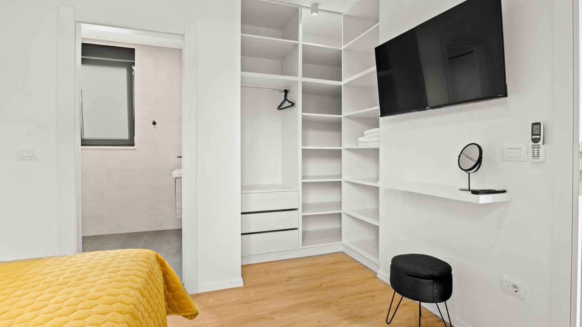 Une chambre à coucher avec un lit, une télévision, une armoire et une salle de bain visible à travers une porte ouverte.