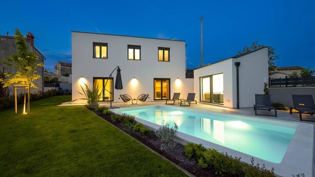 Una casa moderna de dos pisos con piscina, mobiliario exterior y un césped cuidado.