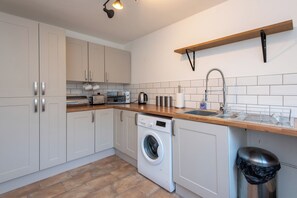A compact kitchen with white cabinets, a washing machine, a sink, and a wooden countertop. - Toast Stays - The Hallington (Newton Aycliffe)