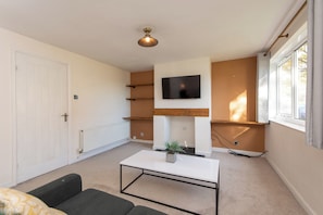 Ein modernes Wohnzimmer mit weißem Couchtisch, einer Couch, einem Kamin und einem an der Wand montierten Fernseher.