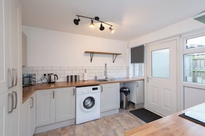 A modern kitchen with white cabinets, a built-in washing machine, a wooden countertop, and a hanging light fixture. - Toast Stays - The Hallington (Newton Aycliffe)