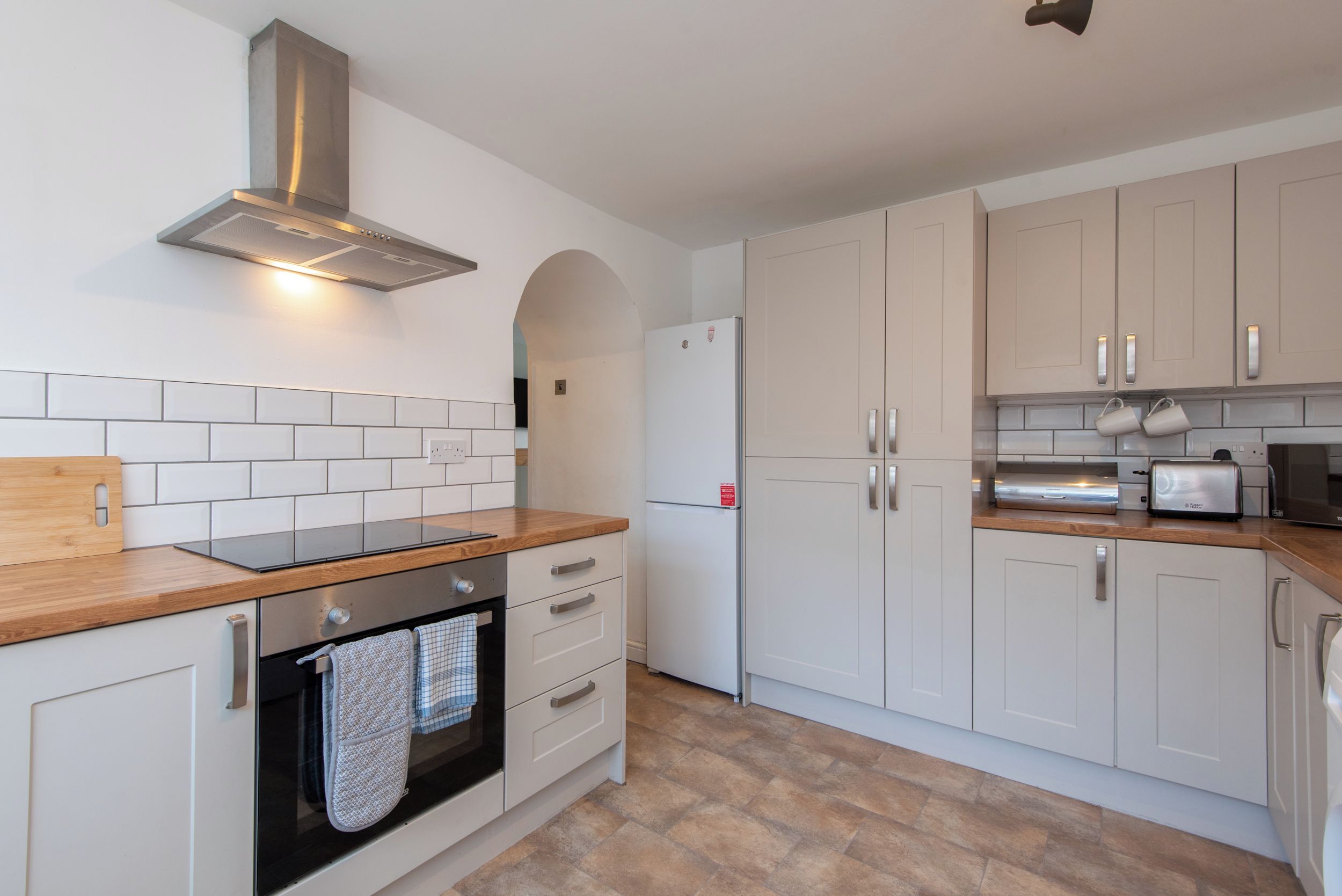 A modern kitchen with white cabinets, a stainless steel range hood, a built-in oven, and a countertop with a wooden cutting board.