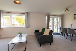 A living room with a sofa, a coffee table, and a dining area with chairs. - Toast Stays - The Hallington (Newton Aycliffe)