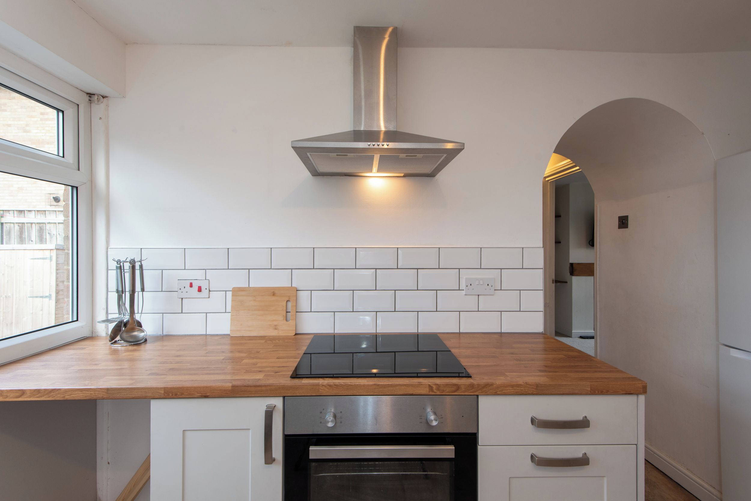 A modern kitchen with a stainless steel range hood, a black induction cooktop, and white cabinetry.