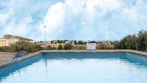 Una piscina con un cartel que indica propiedad privada, vistas a una colina y un área cercada con edificios al fondo.