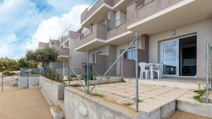 Un edificio residencial con varios balcones, un acceso con portón y un pequeño espacio al aire libre para sentarse.