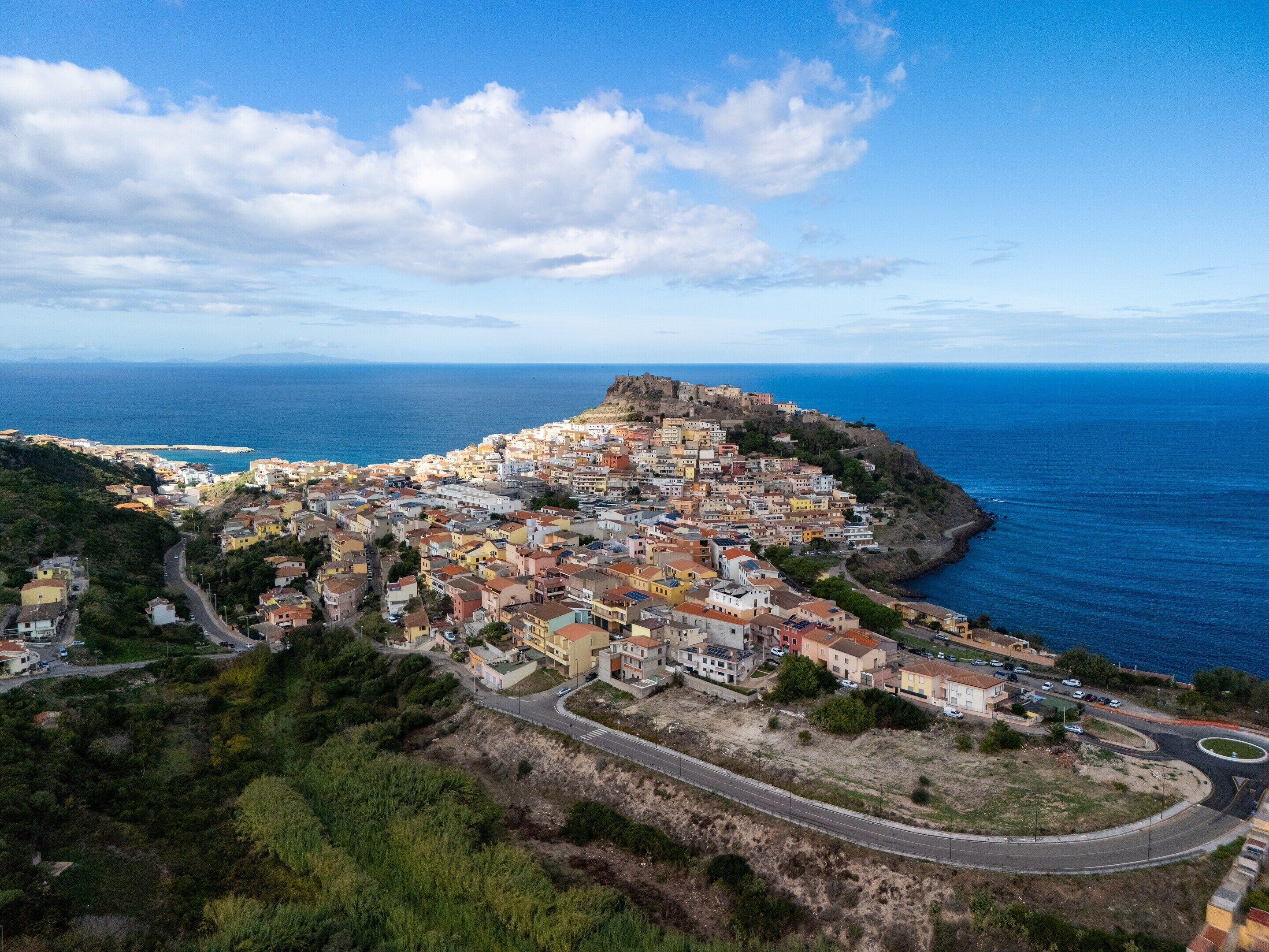 A coastal town with a prominent hilltop fortress, winding roads, and a mix of residential buildings.