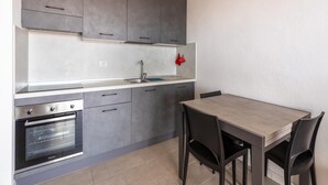 Una cocina moderna con armarios grises, un horno de acero inoxidable, un lavamanos y una mesa de comedor con sillas.