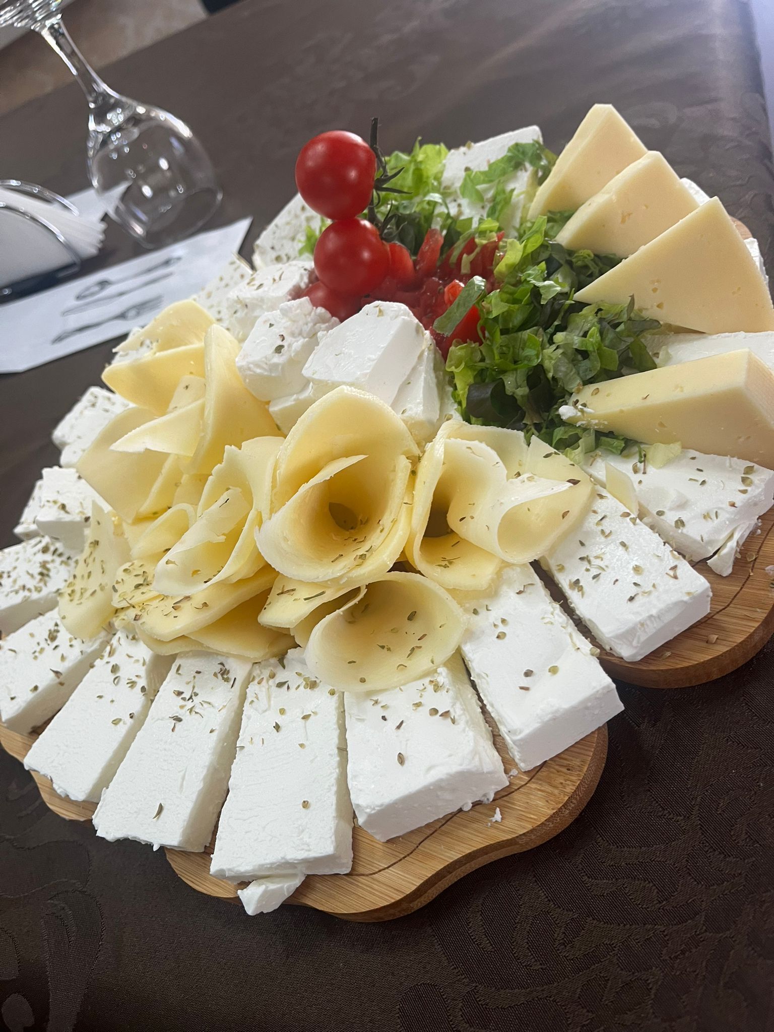 A cheese platter with various types of cheese, cherry tomatoes, and leafy greens on a wooden board.