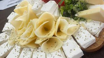 A cheese platter with various types of cheese, cherry tomatoes, and leafy greens on a wooden board.