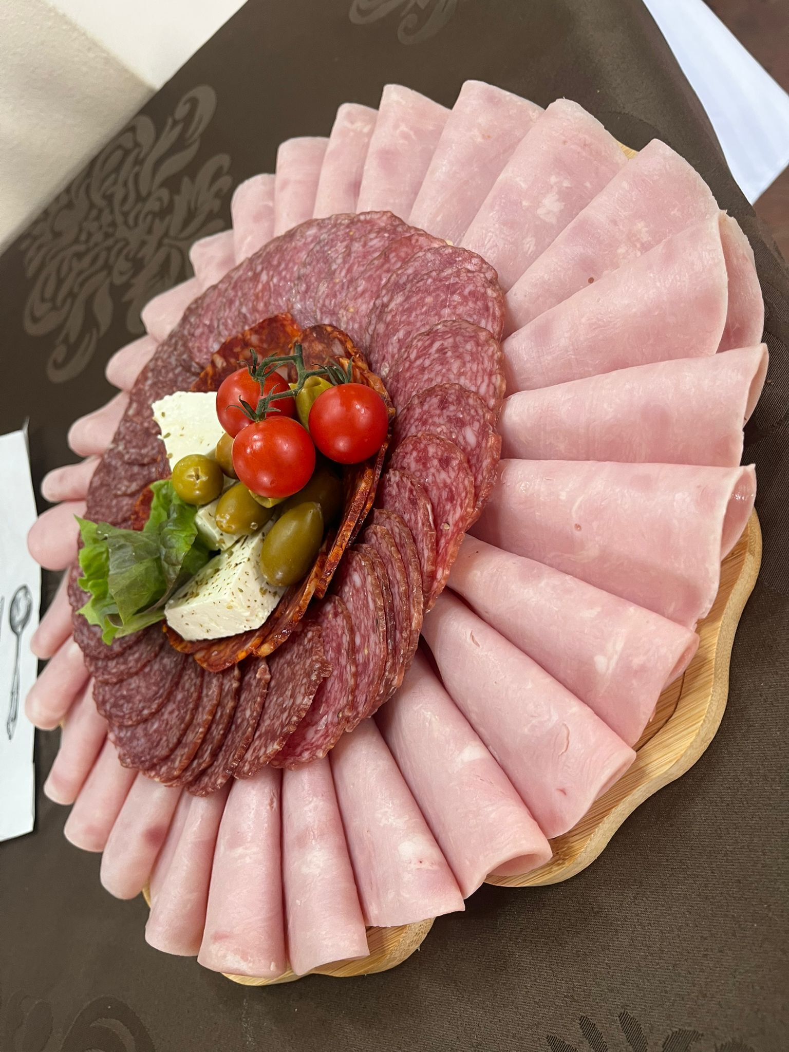 A platter of sliced meats and cheeses arranged in a circular pattern on a wooden board.