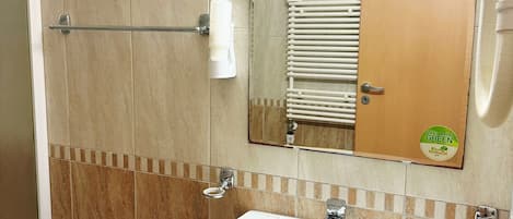 Un baño con lavamanos blanco, un espejo y un perchero para toallas.