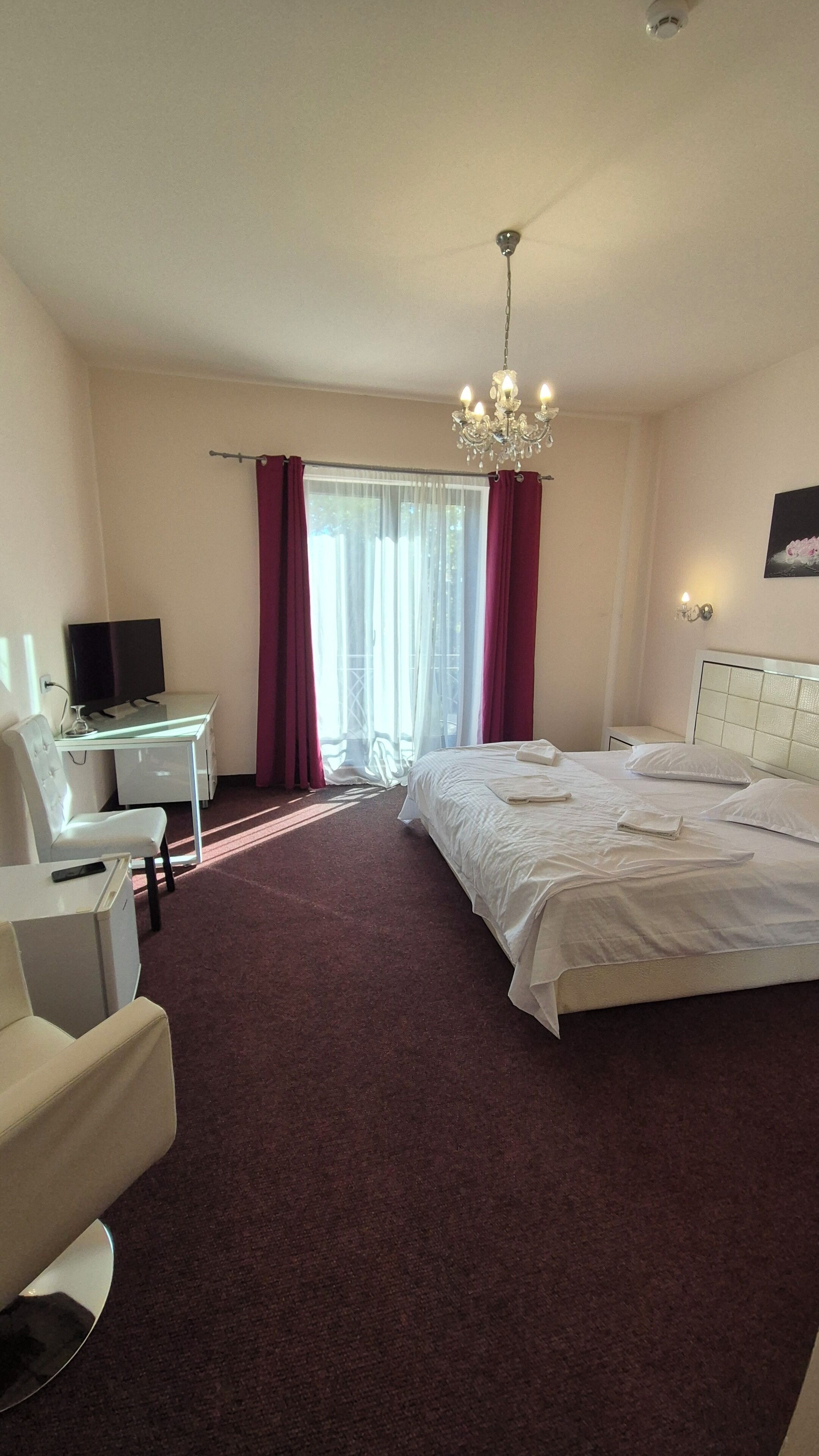 Ein Hotelzimmer mit Bett, Schreibtisch mit Computer, Stuhl, Fernseher und einer Chandelier.