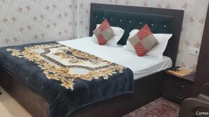 A neatly made bed with a patterned bedspread, two pillows, and a bedside table with a lamp. - Shree Radharaman Palace (Ayodhya)