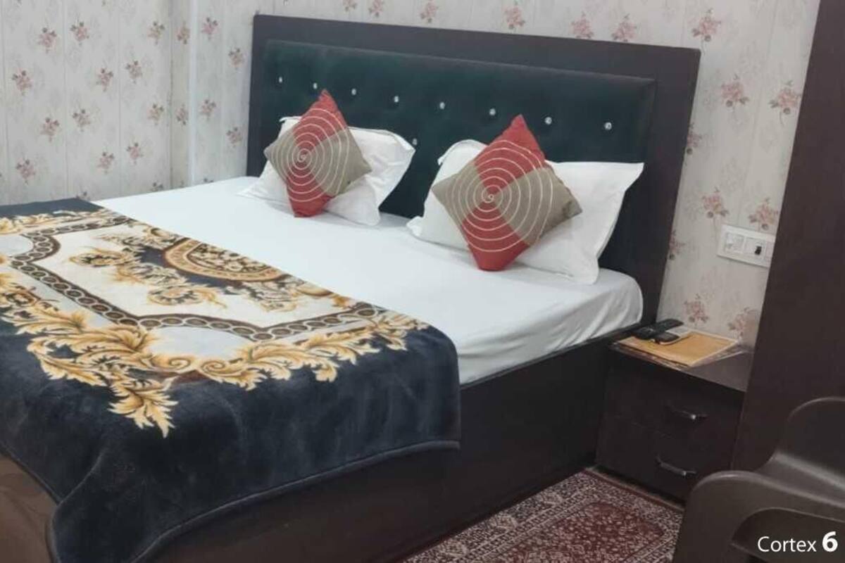 A neatly made bed with a patterned bedspread, two pillows, and a bedside table with a lamp.