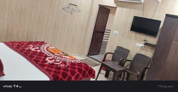 A hotel room with a bed, a TV, a small table, and two chairs. - Shree Radharaman Palace (Ayodhya)