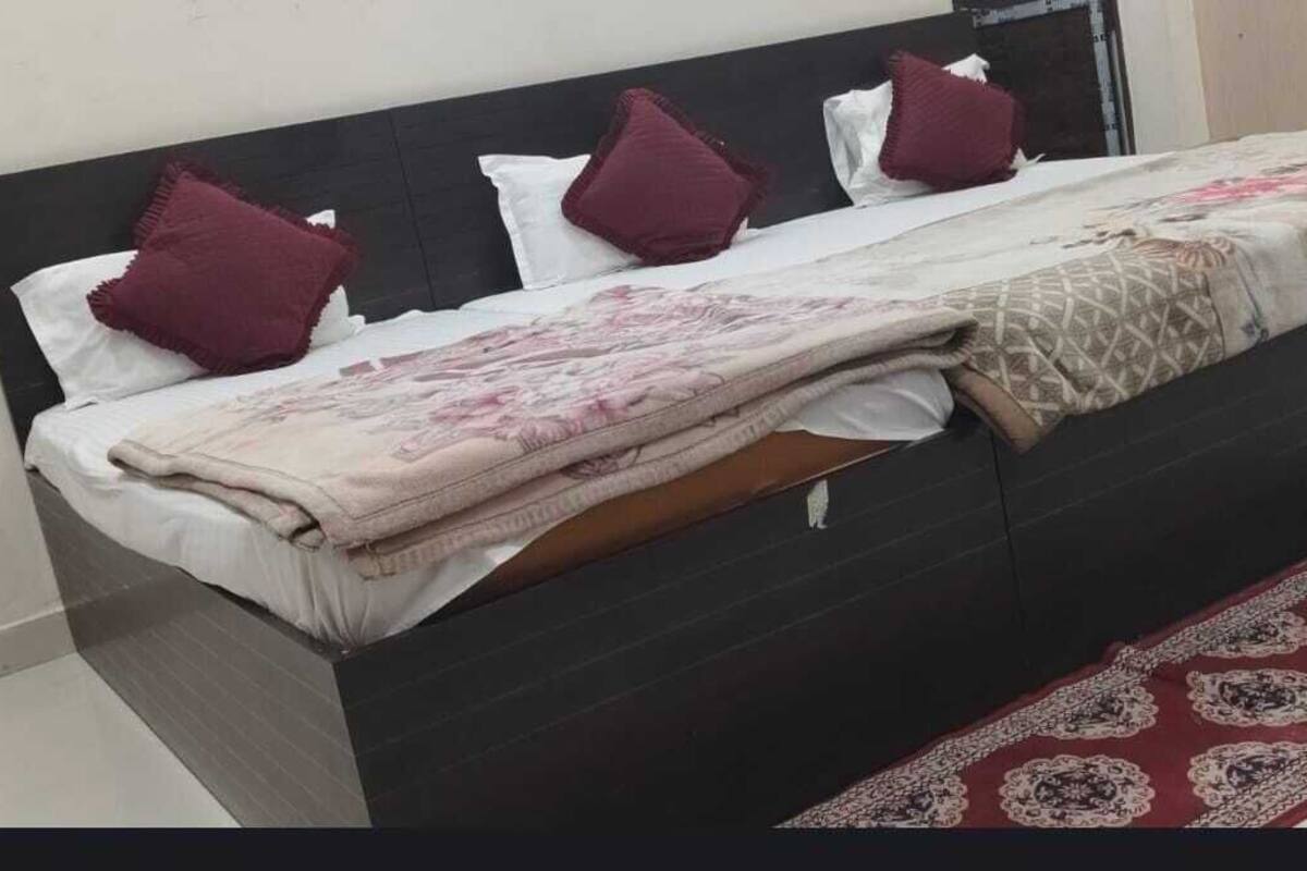 A bed with a dark headboard, white bedding, and a patterned blanket. A red and white patterned rug is on the floor.