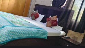 A bed with a patterned bedspread, pillows, and a bedside table with a remote control. - Shree Radharaman Palace (Ayodhya)