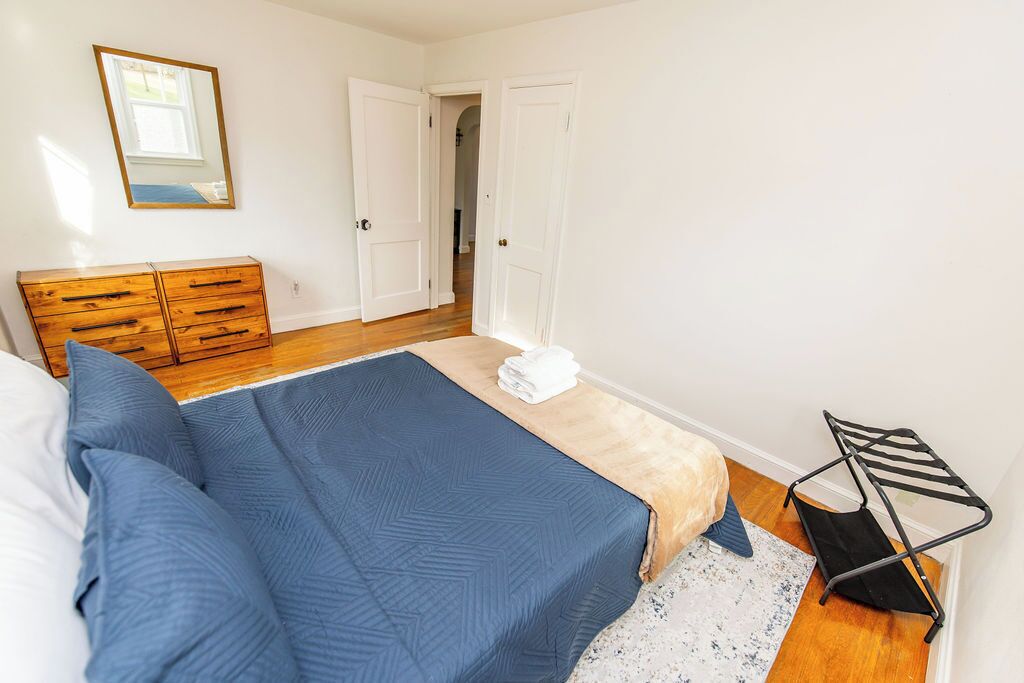 A bedroom with a bed, a wooden dresser, a mirror, and a door leading to another room.