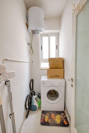 Ein kleiner Hauswirtschaftsraum mit Waschmaschine, Staubsauger und Warmwasserbereiter.