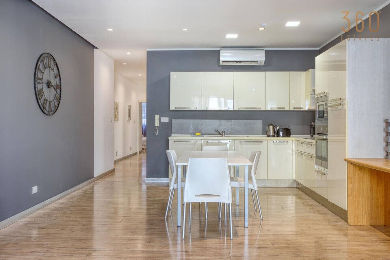 Une cuisine moderne avec des meubles blancs, un îlot central et un coin repas avec des chaises blanches.