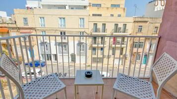 Un balcon avec deux chaises en métal et une petite table, donnant sur un quartier résidentiel composé de plusieurs immeubles.